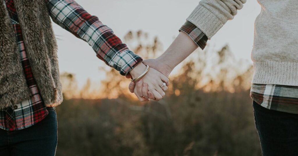 Husband and wife holding hands while standing apart, trying to resolve conflict in their marriage