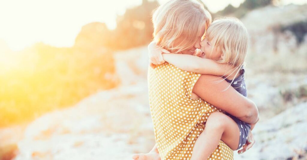 mom hugging her daughter and laughing with her, on the beach