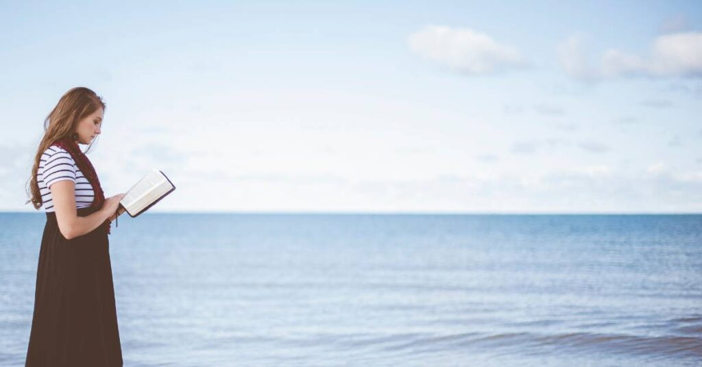 woman reading her Bible and walking along the beach by the ocean