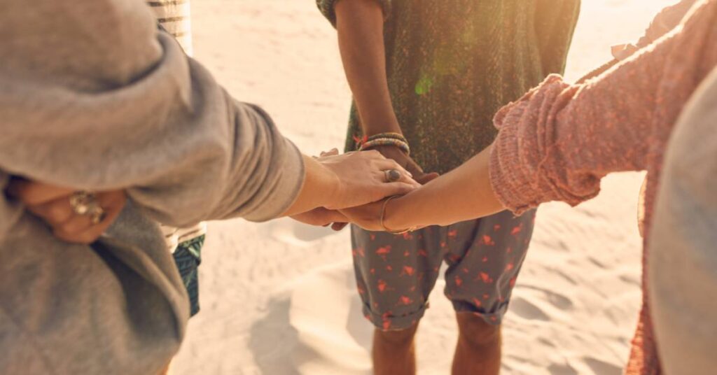 three friends holding hands on the beach offering each other mom coach encouragement and support