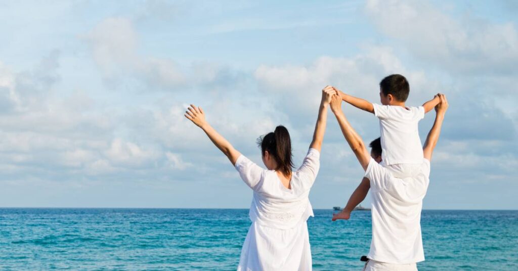 Christian family standing by the ocean with their arms raised high in worship