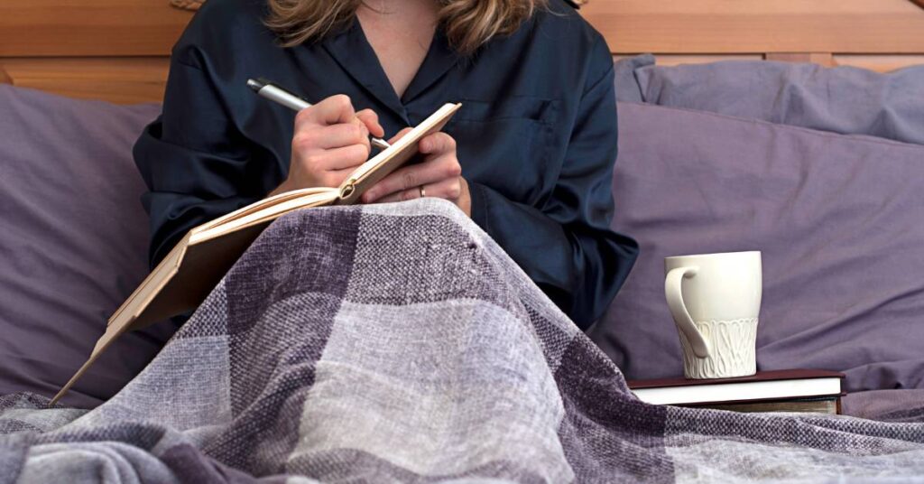 mom sitting in bed with a cup of tea, journaling her year end reflections