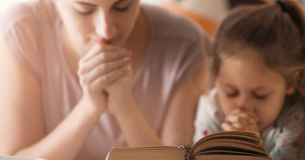 close up photo of Mom and Daughter praying together while reading the Bible in faith-based parenting